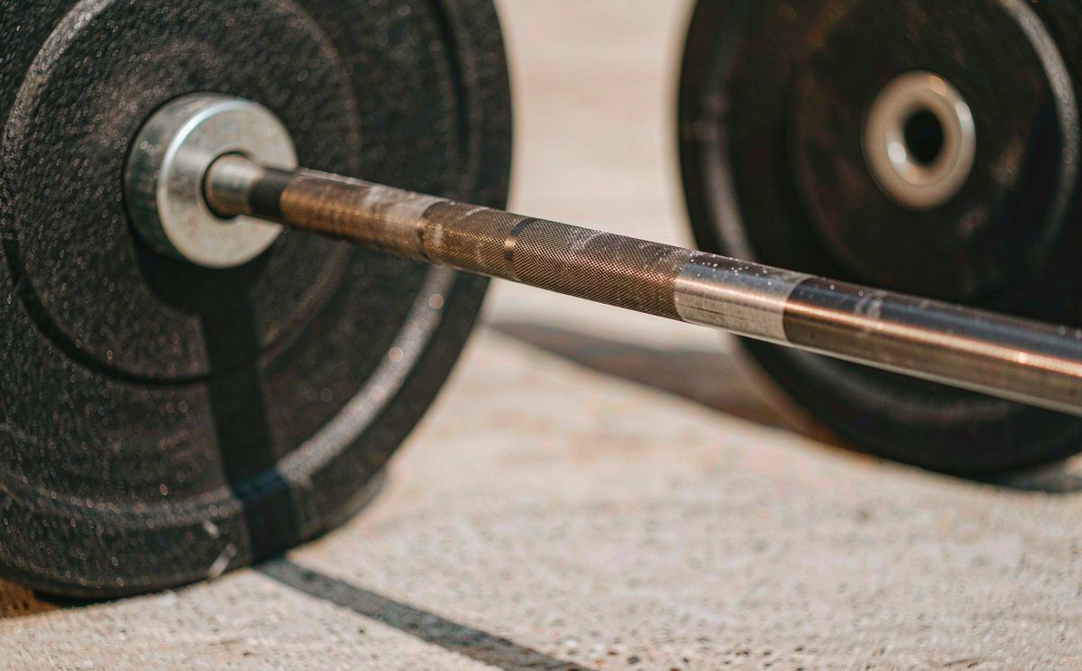 Close-up of the knurled shaft of an Xiaole Olympic barbell resting on concrete, with bumper plates blurred behind.