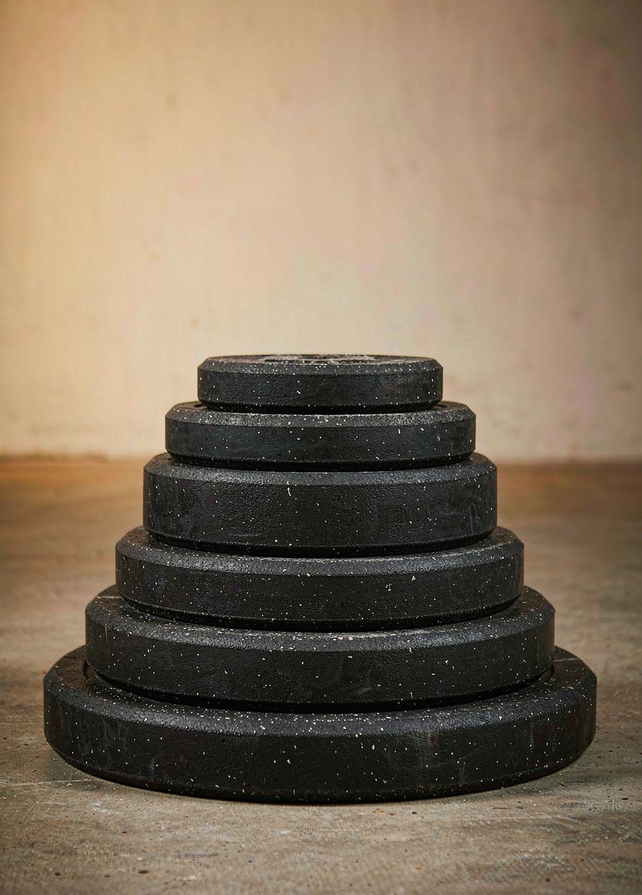 A stack of six black rubber bumper plates of descending size on a concrete floor.